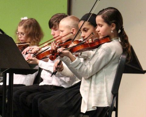 Students playing their violins during an orchestra concert.