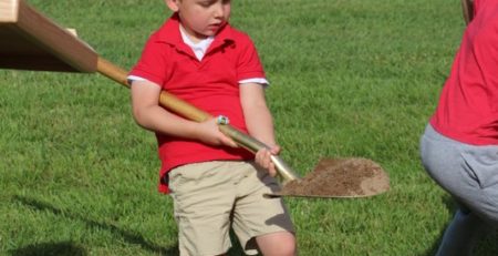 Student with a shovel and dirt at the ground breaking ceremony at the new school property.