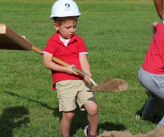 Student with a shovel and dirt at the ground breaking ceremony at the new school property.