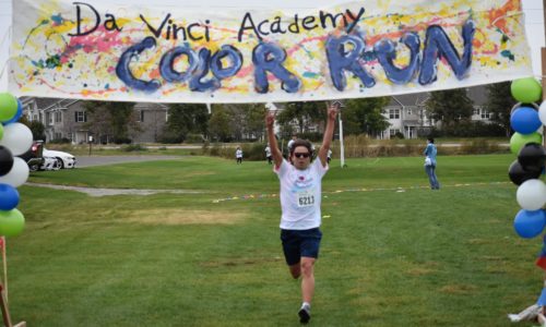 Alumni student running through the finish line at the school's color run.