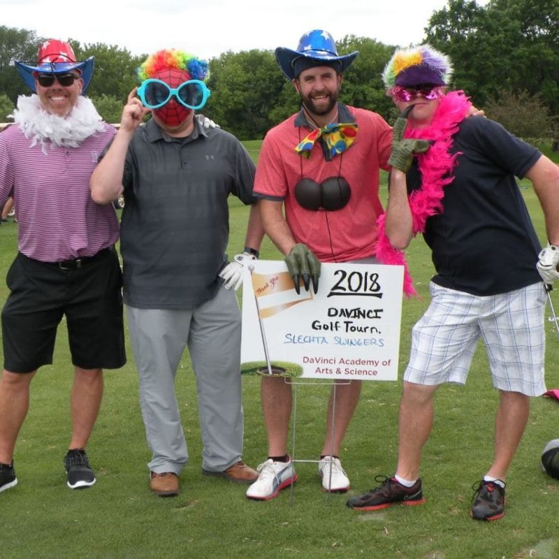 Men golfers dressed up in hats and wigs