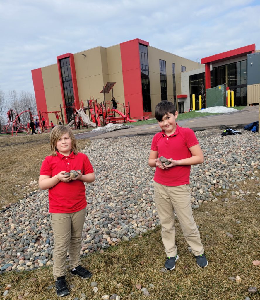 Two students from Ms. Meyer's fifth grade class spending recess time putting rocks back into the landscaping.